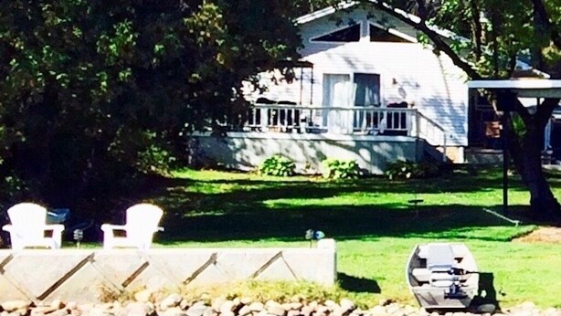 A lakeside house with a dock, a lawn, and a small boat. - Lake Front Chalet (Queensbury)