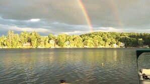A lake with a rainbow, a boat, and a forested shoreline. - Lake Front Chalet (Queensbury)