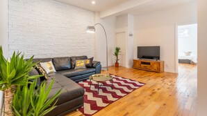 Een moderne woonkamer met een modulaire bank, een televisie op een houten dressoir, een rood-wit gestreept vloerkleed en een potplant.