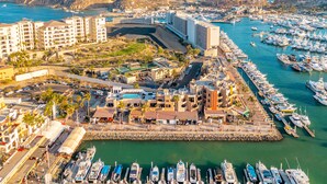A marina with numerous boats docked, a large building with a curved structure, and a mountainous backdrop.