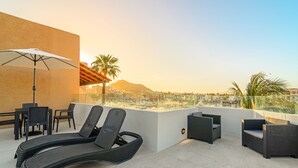A rooftop terrace with lounge chairs, a table, and an umbrella.