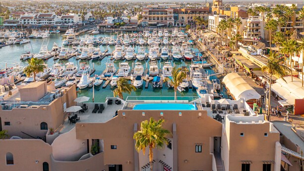 A marina with numerous boats docked, surrounded by buildings with balconies and palm trees.