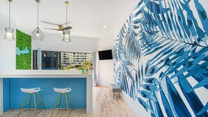 A modern kitchen with a blue bar area, two white bar stools, a green wall, and a large blue leaf-patterned wall.