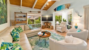A spacious living room with a wooden ceiling, a large sofa, a coffee table, and a view of the outdoors. - High-End Oceanfront Sanctuary with Upgraded Luxury Interior (Kailua Kona)
