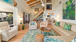 A spacious living area with a high ceiling, a staircase, and a kitchen in the background. - High-End Oceanfront Sanctuary with Upgraded Luxury Interior (Kailua Kona)