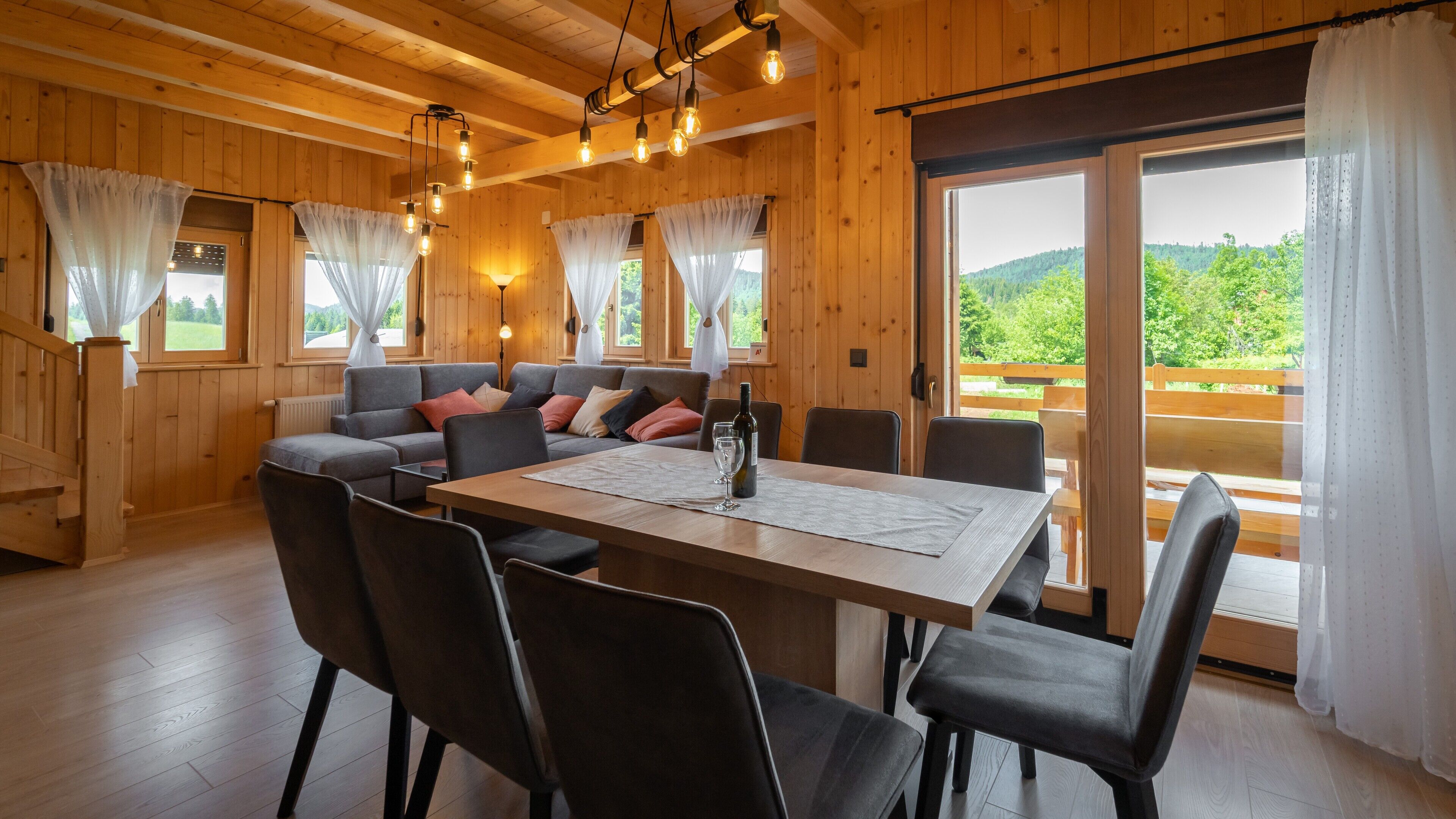 A wooden interior with a dining table, chairs, a sofa, and curtains.