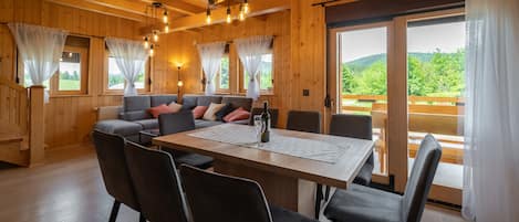 A wooden interior with a dining table, chairs, a sofa, and curtains.