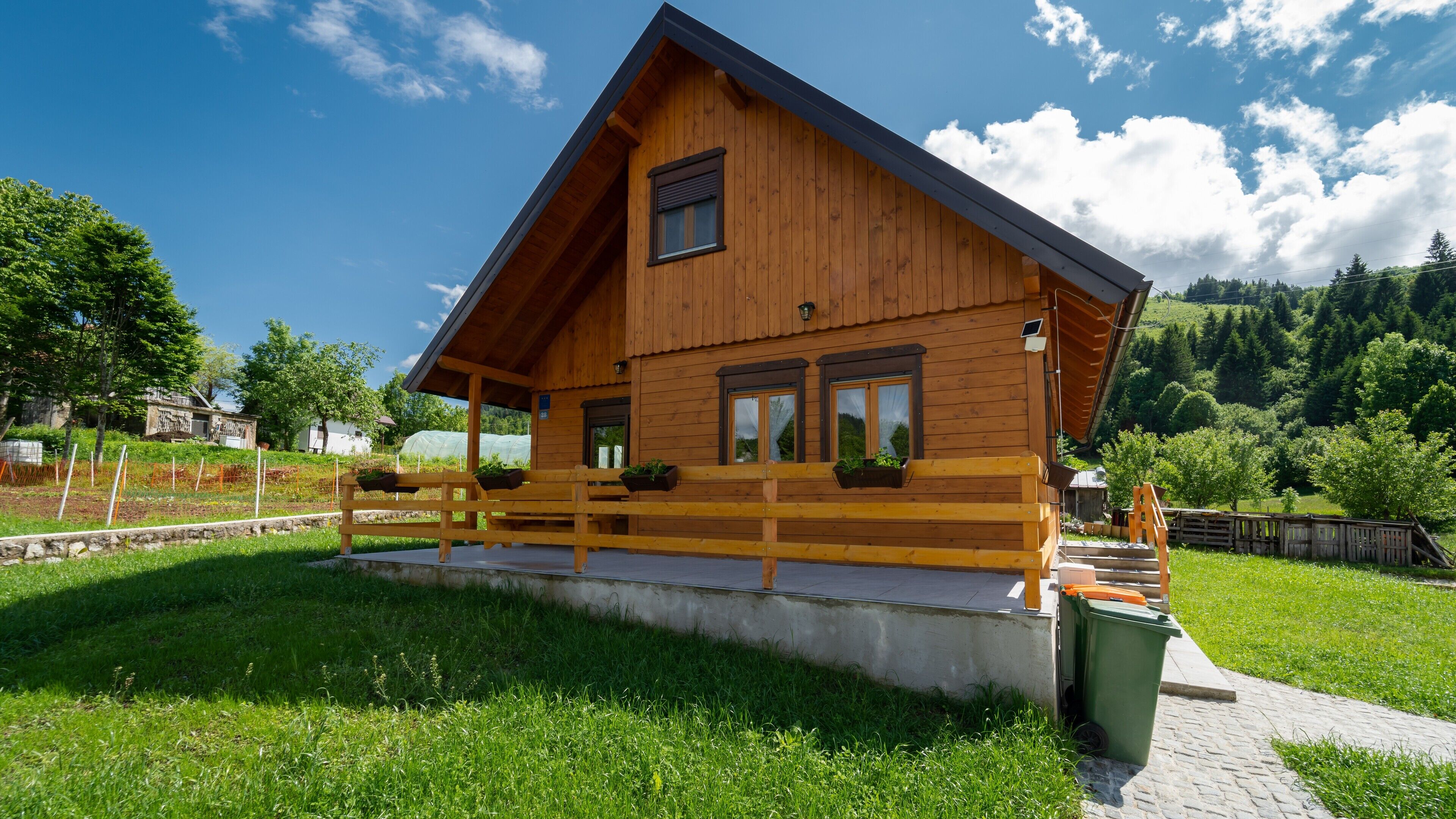 Eine Holzhütte mit geneigtem Dach, einer Veranda mit Bänken und Blick auf eine grüne Landschaft.