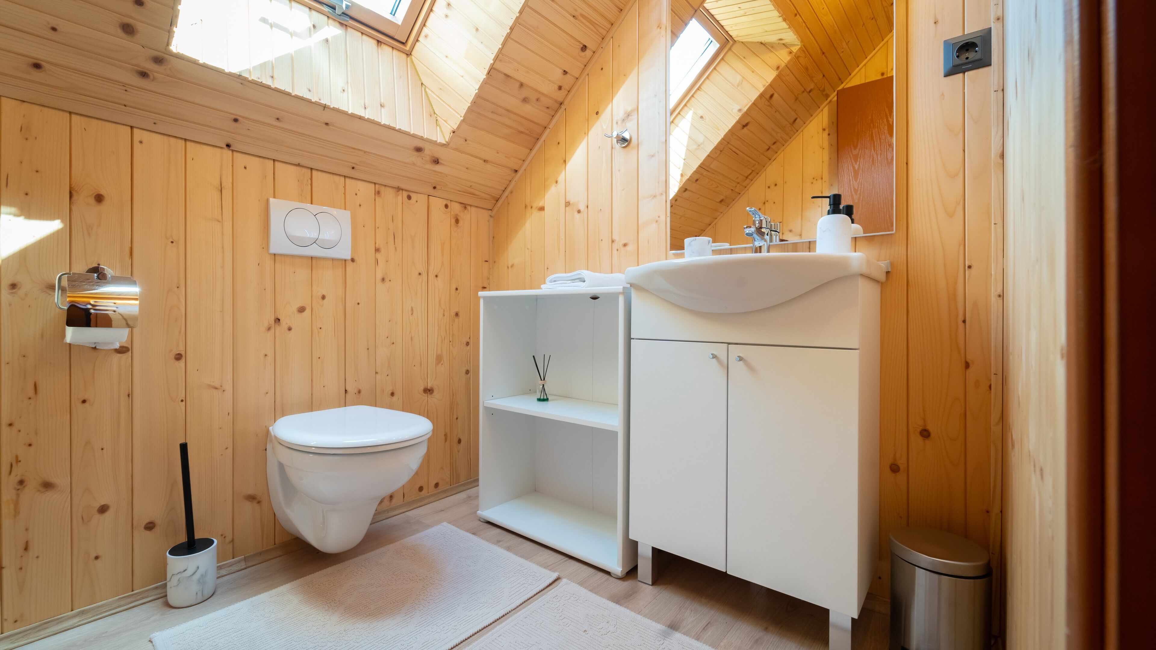 A compact, wooden-paneled bathroom with a white toilet, a sink, and a small shelf.