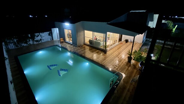 A swimming pool with a wooden deck and a glass-enclosed patio area. - GoBravo 71: 2Bhk Farm with Pool & Garden Sector 150 Noida (Noida)