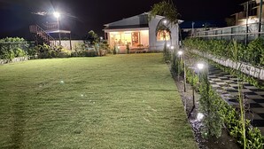 A well-lit residential property at night with a neatly maintained lawn, a small garden area, and a paved walkway. - GoBravo 71: 2Bhk Farm with Pool & Garden Sector 150 Noida (Noida)