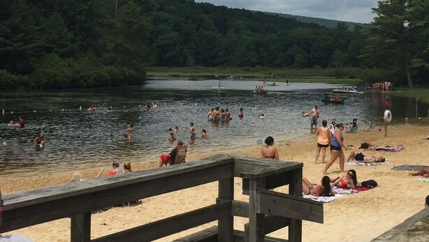 Una playa junto al lago, con gente nadando y descansando sobre la arena.