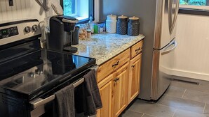 Una cocina moderna con horno empotrado, microondas y refrigerador. Cuenta con gabinetes de madera, encimera de granito y una ventana que proporciona luz natural.