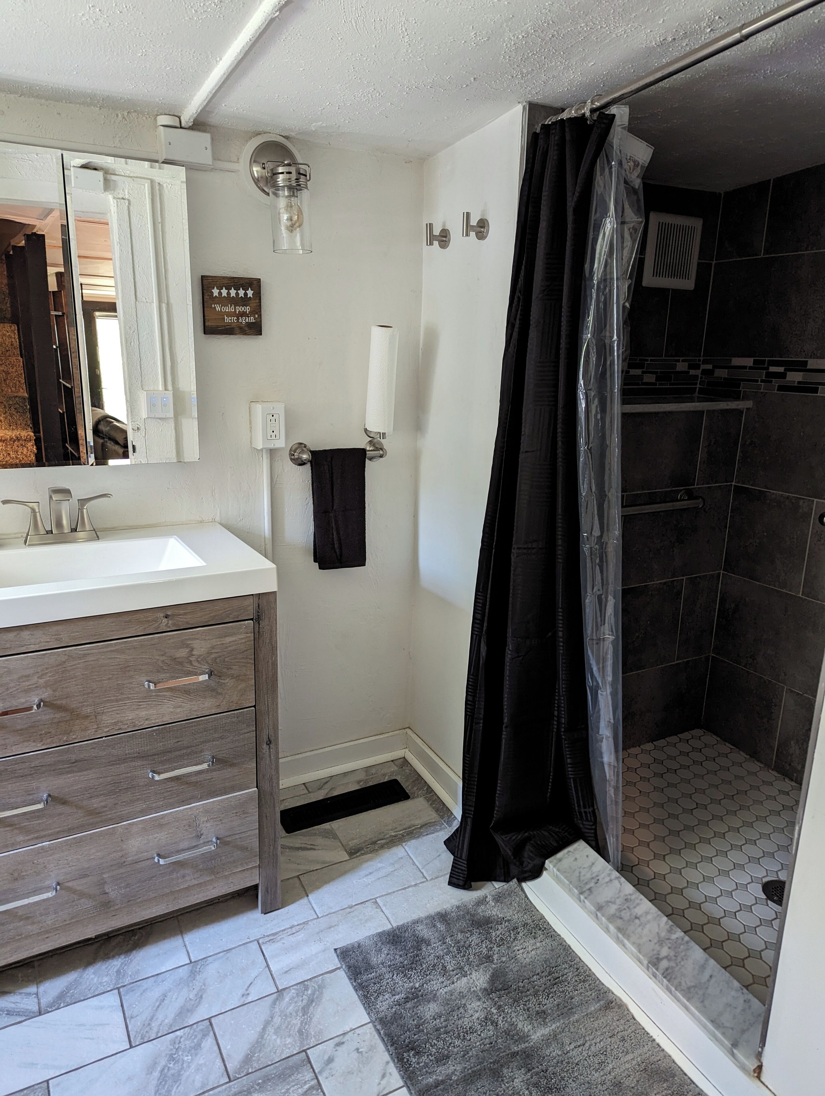 A bathroom with a white vanity, a shower with a black curtain, and a tiled floor.
