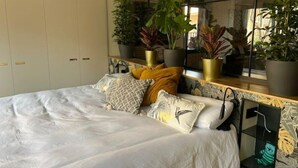 Een slaapkamer met een bed, verschillende potplanten en een raam.