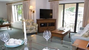 Ein Hotelzimmer mit Fernseher, einem Glastisch gedeckt mit Kerze, Weingläsern und einer Couch.