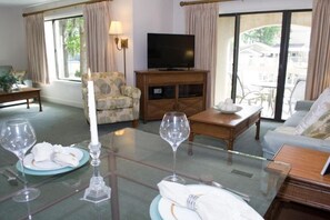 A hotel room with a television, a glass table set with a candle, wine glasses, and a sofa.