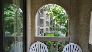 Ein Steine Balkon mit zwei weißen Plastikstühlen, mit Blick auf ein Wohngebiet mit einem Haus und Grünflächen.