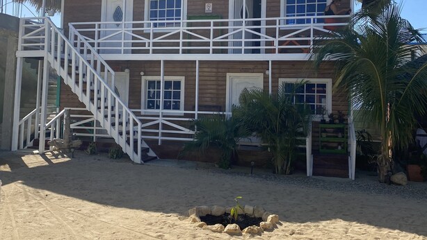 A two-story wooden building with a balcony, a staircase, and a sandy ground area. - Ocean front. Kiters hotel (Buen Hombre)
