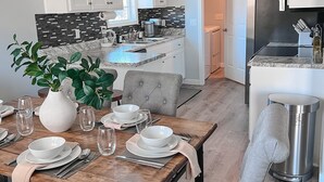 Une cuisine moderne avec des meubles blancs, un plan de travail noir et un coin repas doté d’une table en bois, mise pour quatre personnes.