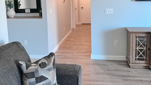 Un salon moderne avec un canapé gris, un coussin décoratif à motifs, un grand miroir et un téléviseur à écran plat fixé au mur.