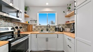 Une cuisine moderne avec des meubles blancs, un four à micro-ondes en acier inoxydable et une fenêtre au-dessus de l’évier.