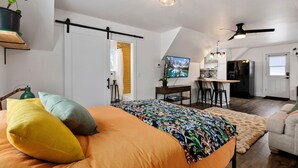 Une chambre avec un lit, un bureau et un coin cuisine à l’arrière-plan.