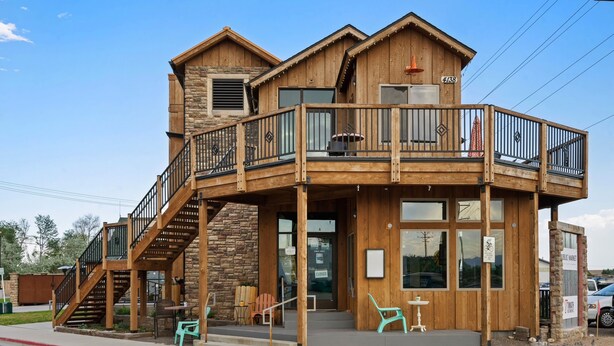 Un bâtiment en bois à deux étages, doté d’un balcon, d’un escalier et d’un espace extérieur aménagé pour s’asseoir.