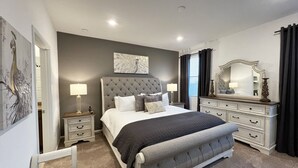 A bedroom with a large bed, two bedside tables with lamps, a dresser, and artwork on the walls.