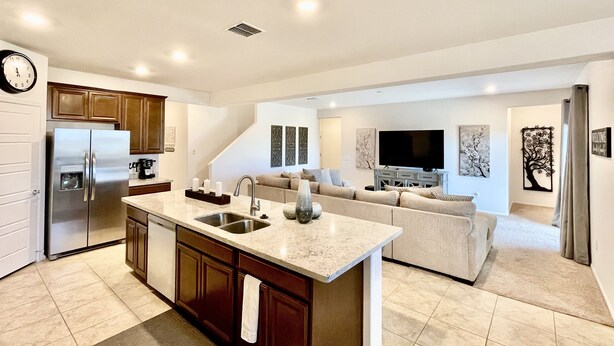 A modern kitchen with a built-in island, stainless steel appliances, and a dining area with a sofa and flat-screen TV.