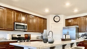 A kitchen with wooden cabinets, a stainless steel refrigerator, a microwave, and a large island with bar stools.
