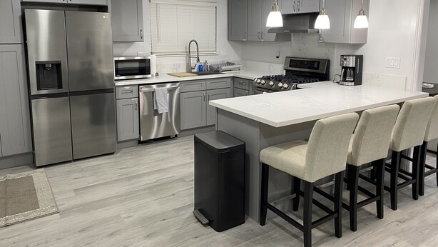 A modern kitchen with stainless steel appliances, a central island with bar stools, and pendant lighting. - PickleballShopsFoodies 5Bedrms 2Washers 3Dryers (Montclair)