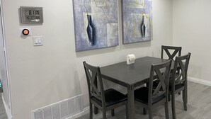 A dining area with a table and four chairs, two wall-mounted paintings, a thermostat, and a light switch. - PickleballShopsFoodies 5Bedrms 2Washers 3Dryers (Montclair)