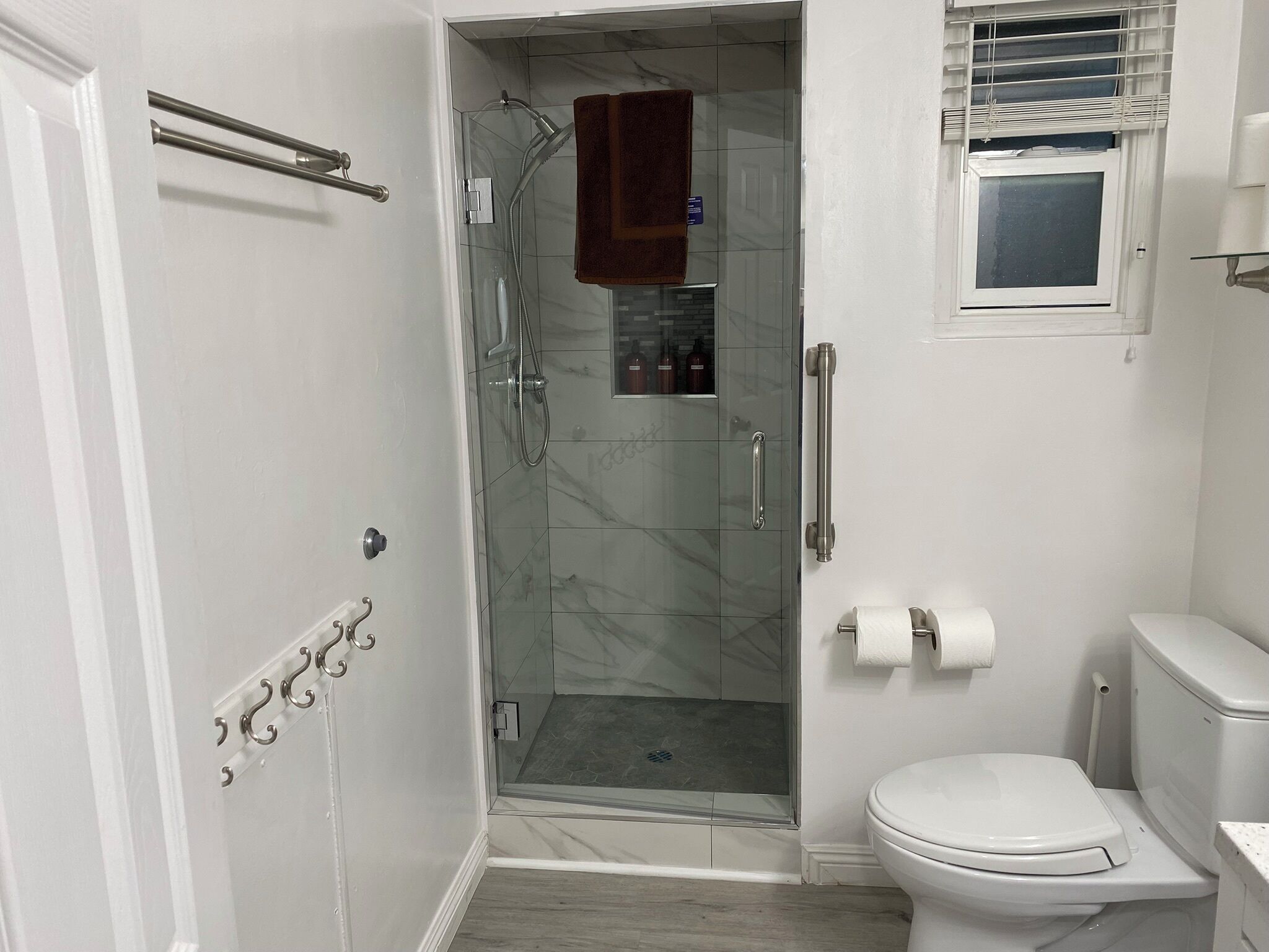 A bathroom with a glass-enclosed shower, a toilet, and a small window.