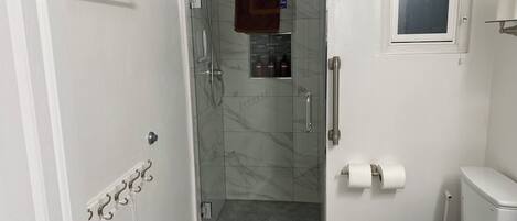 A bathroom with a glass-enclosed shower, a toilet, and a small window.