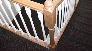 A wooden staircase with white balusters and a handrail, leading to a door with a glass panel and an exit sign. - Rewak Studios (Fairbanks)
