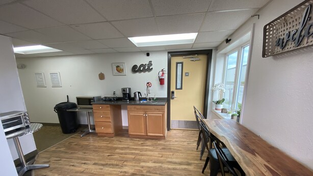 A kitchen area with a wooden countertop, a sink, and a stove. There is a trash can and a window with a view of the outside. - Rewak Studios (Fairbanks)