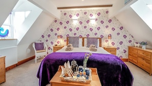 A bedroom with a sloped ceiling, a bed with a purple bedspread, a wooden nightstand, a chair, and a dresser. - Nobles Cottage - UK43351 (Whitby)