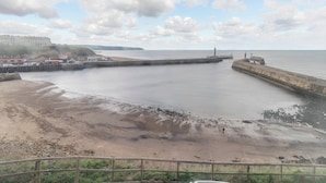 A coastal view with a sandy beach, a pier, and a lighthouse. - Nobles Cottage - UK43351 (Whitby)