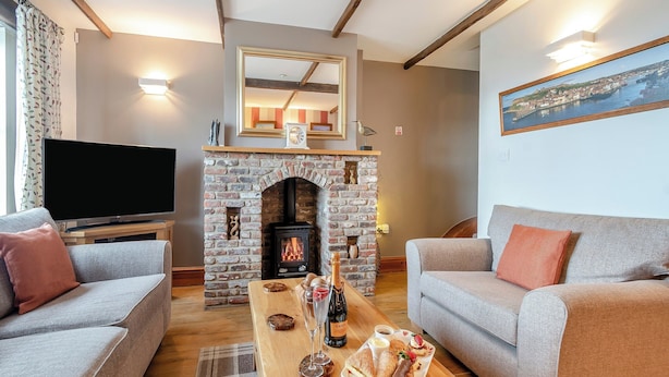 A cozy living room with a fireplace, two grey sofas, a wooden coffee table with snacks, and a flat-screen TV. - Nobles Cottage - UK43351 (Whitby)