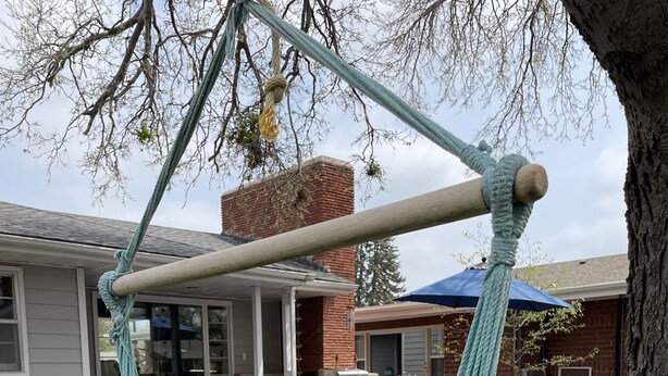 Una hamaca colgada entre dos árboles en un patio trasero con terraza, muebles de exterior y una parrilla.