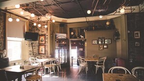 L’intérieur d’un restaurant avec des tables et des chaises en bois, un mur en pierre et des luminaires suspendus.