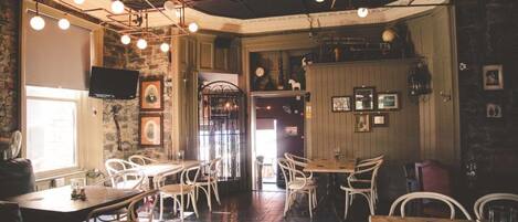 A restaurant interior with wooden tables and chairs, a stone wall, and hanging lights.