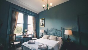 Une chambre à coucher avec un grand lit, deux tables de chevet avec des lampes, une chaise, une fenêtre avec des rideaux et un lustre.