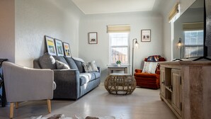 A living room with a grey sofa, a red armchair, a wooden cabinet, and a cowhide rug. - Charming Cody Home - sleeps 5, walking distance to downtown! (Cody)