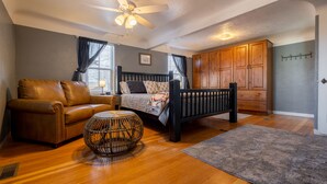 A bedroom with a bed, a leather sofa, a round wicker table, wooden flooring, and a ceiling fan. - Charming Cody Home - sleeps 5, walking distance to downtown! (Cody)