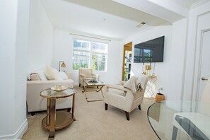 A living room with a sofa, armchair, coffee table, and a TV mounted on the wall.