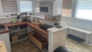 Una cocina compacta con microondas, tostadora y cafetera. Se observan armarios de madera y una encimera con diferentes utensilios de cocina.