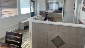 Una cocina moderna con una isla central, un comedor con una mesa y sillas de madera, y un dormitorio con cama y cortinas.