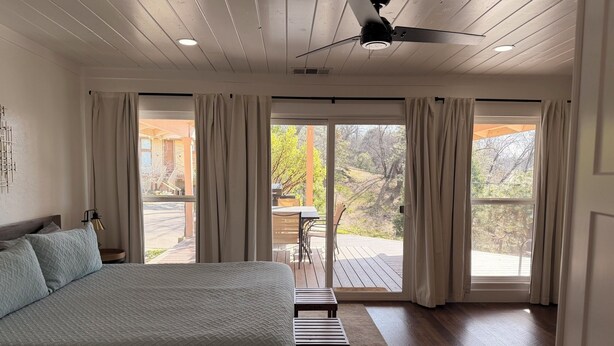 A bedroom with a bed, a ceiling fan, and a view of the outdoors through large windows. - Good Vibes getaway lake views, Marina, private Boat Slip (Bass Lake)